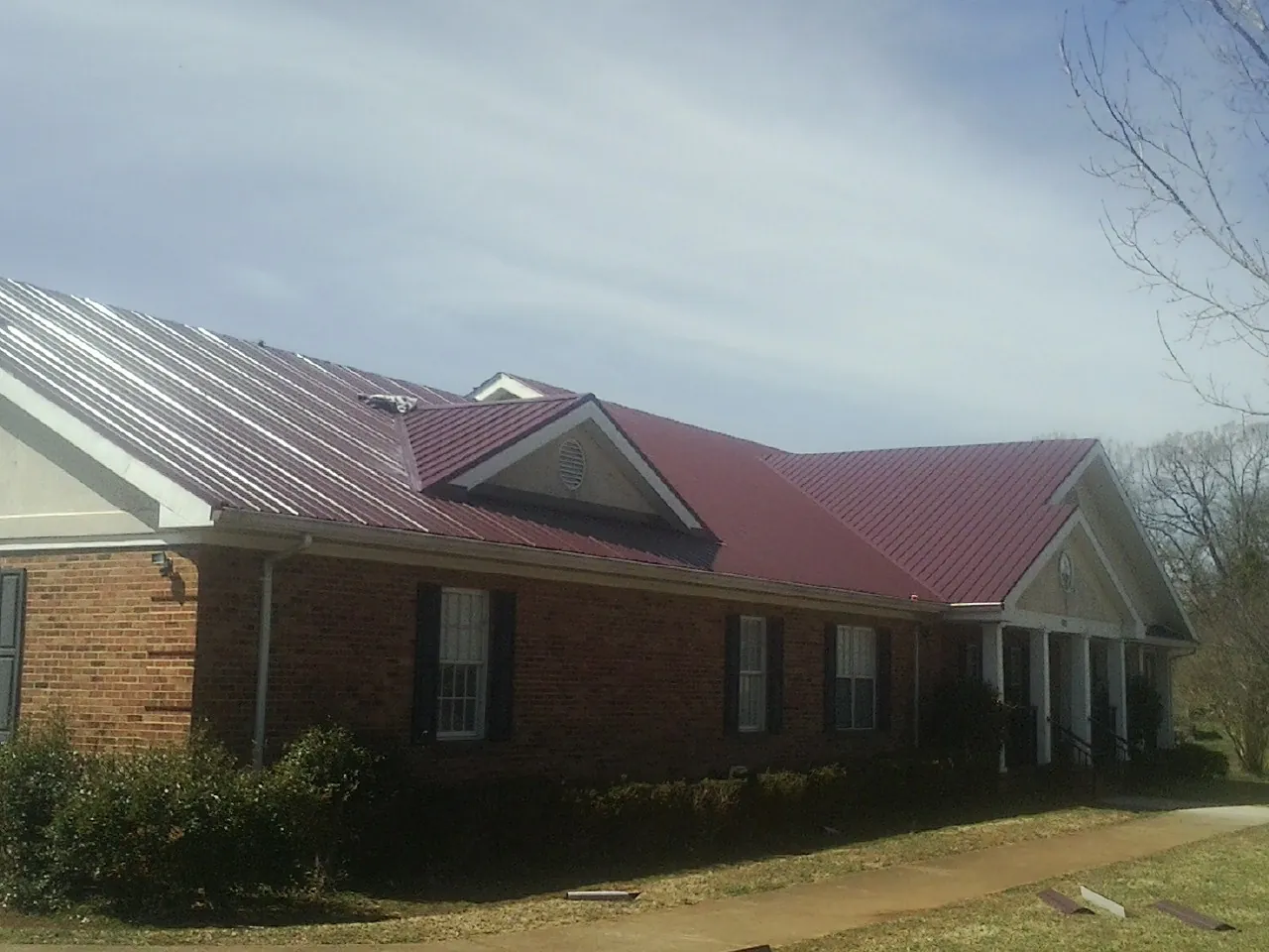 Red metal roof with gabled entries on a long brick building, from a Hail Damage Roof Repair job in Good Thunder