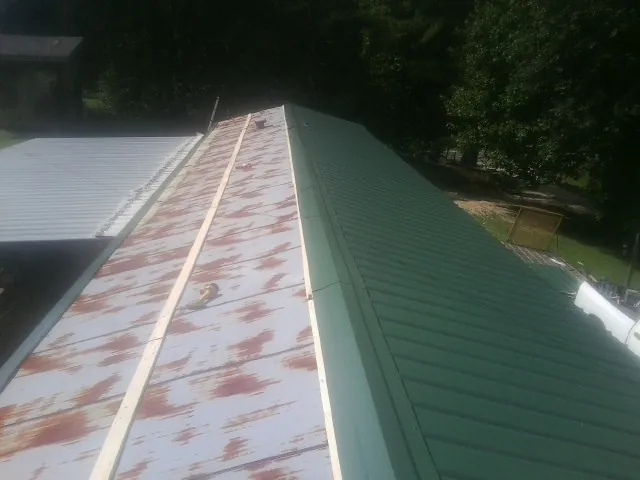 Old rusted panels beside newly installed green metal roofing — Wind Damage Roof Repair by Roofing Brothers in Good Thunder