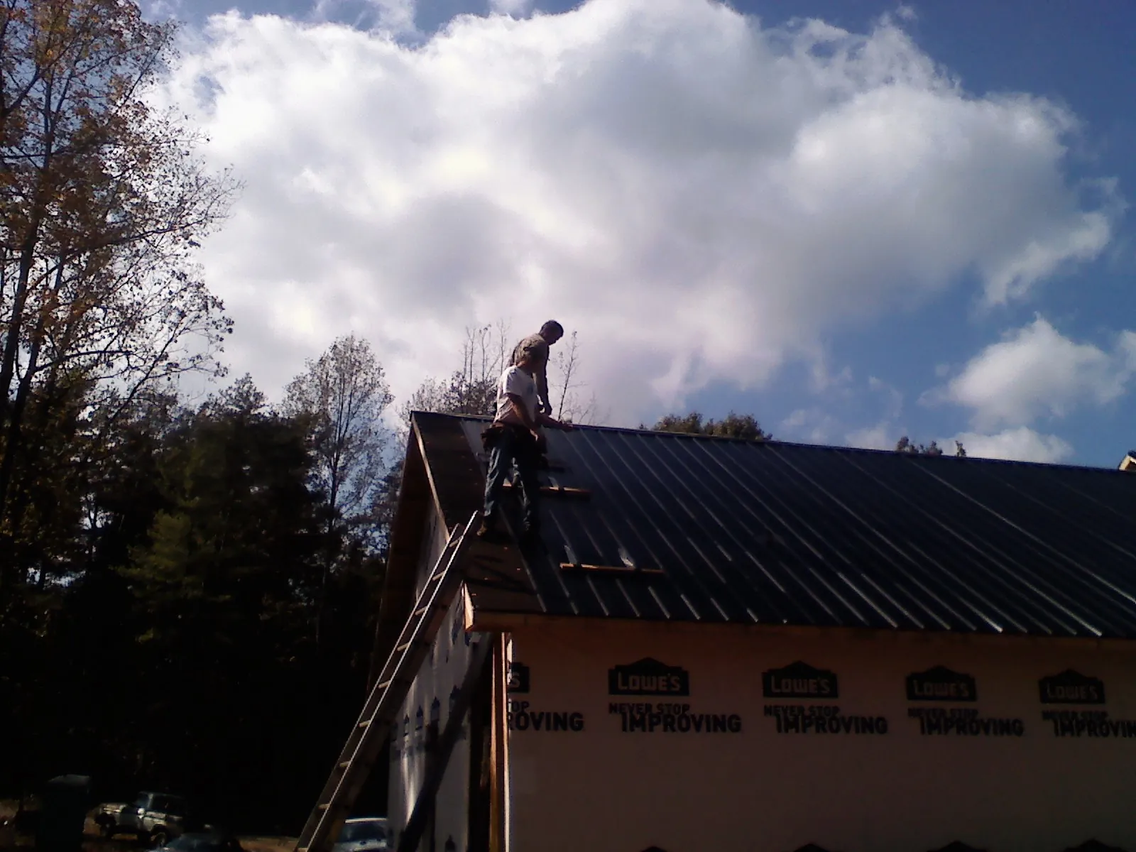 Roofer fastening dark metal panels high against a cloudy sky, from a Roof Inspection job in Good Thunder