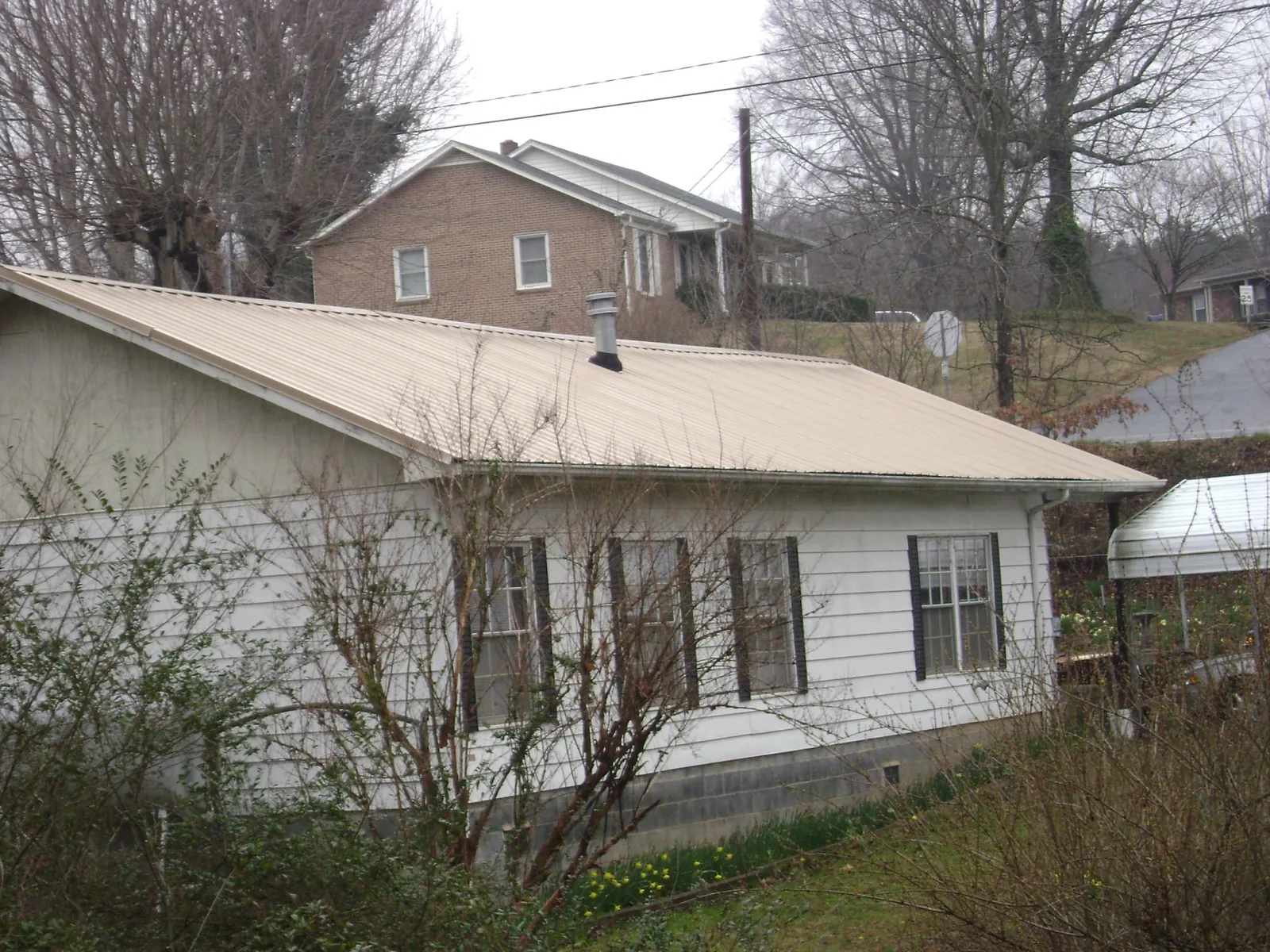 Tan metal roof on a white sided house set into a hillside — Commercial Roofing by Roofing Brothers in Good Thunder